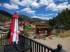 Summer view of the Platinum Chairlift at Red River Ski & Summer Area from a patio deck, featuring a closed red and white umbrella, the lift terminal, and resort lodging against a backdrop of green mountains and blue sky.