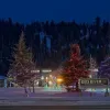 Red River's lit Christmas trees stand in the snow by the town welcome sign at night.