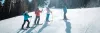 A ski instructor in a red jacket leads a lesson on a groomed slope at Red River Ski and Summer Area.