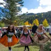 Women in dirndls celebrate at Red River Oktoberfest in Brandenburg Park beneath golden aspens.