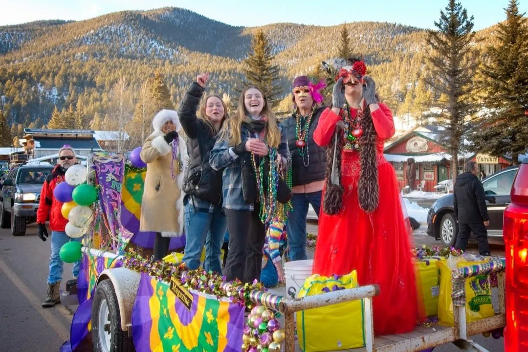 A Mardi Gras krewe queen in a red gown rides a parade float in Red River.