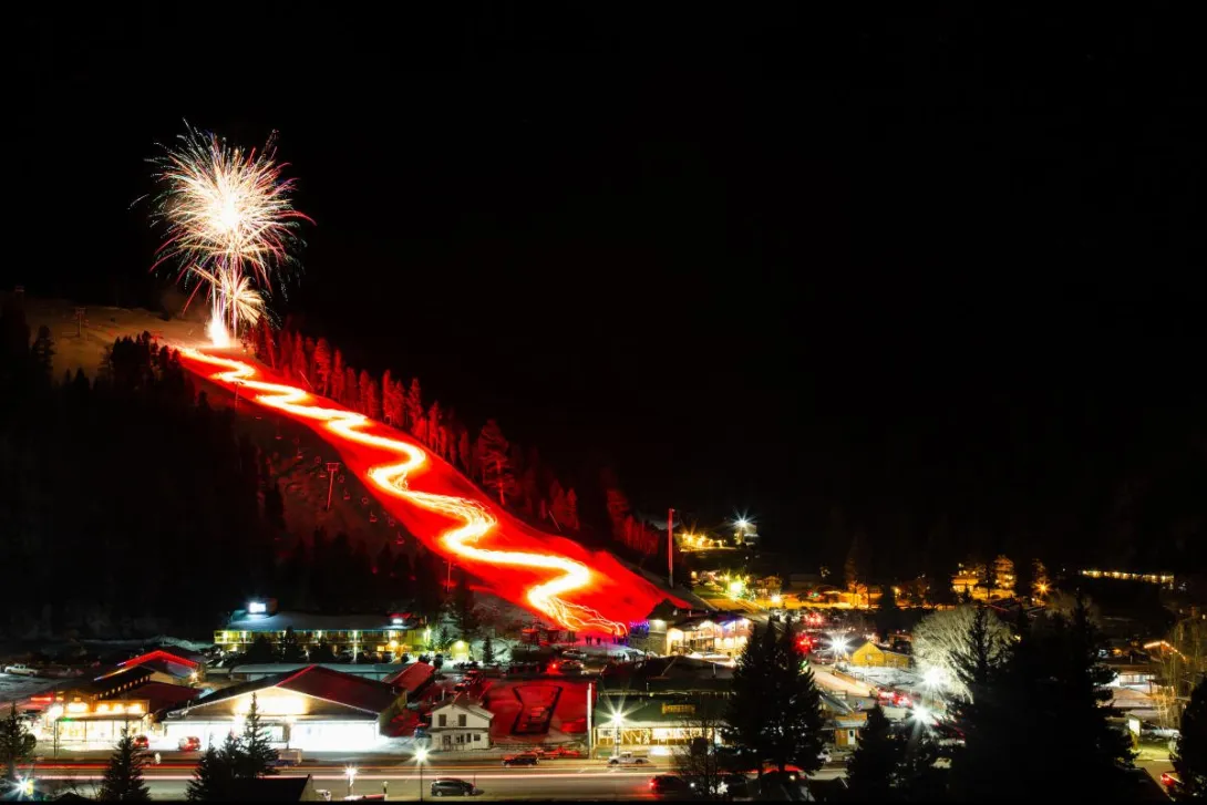 A wide view of the torchlight parade and fireworks over Red River at night.