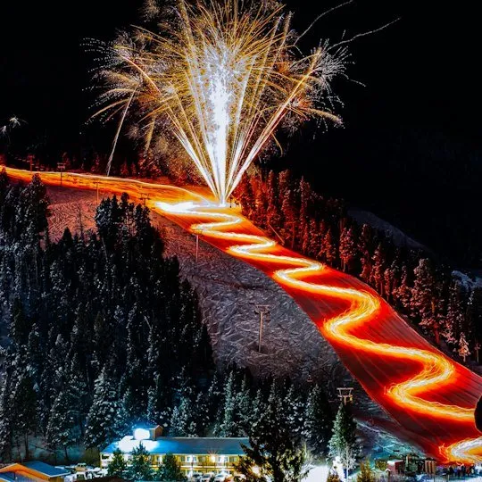 Torchlight trail switchbacks glow beneath fireworks at Red River Ski Area.