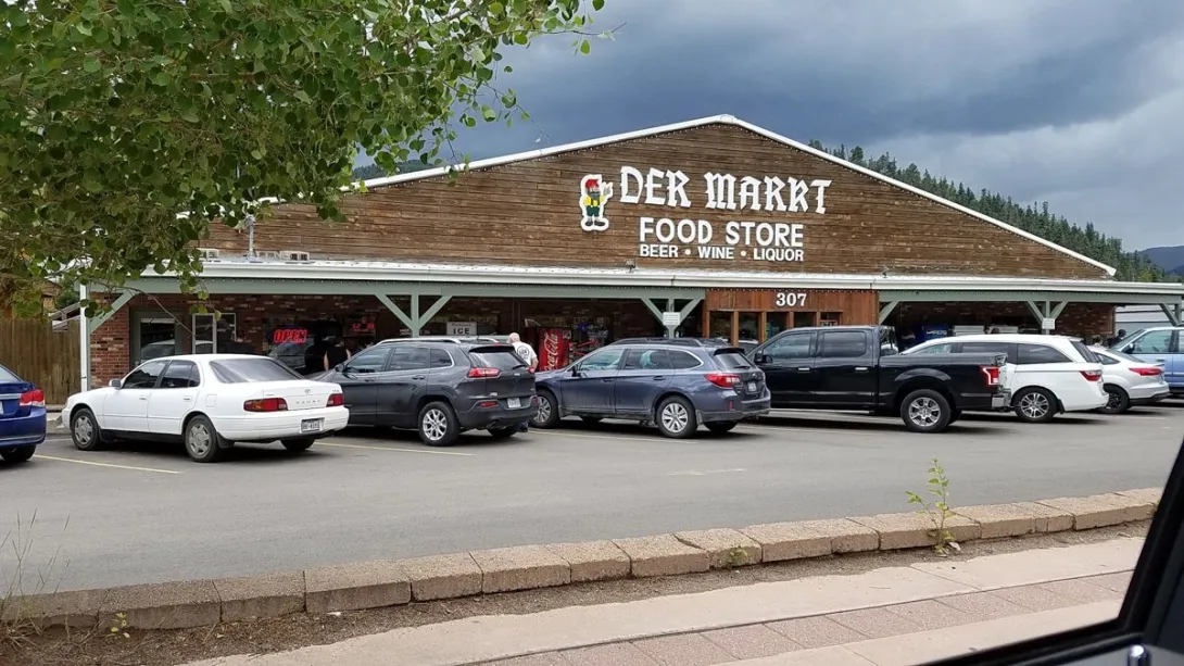 The Der Markt Food Store storefront at 307 West Main Street in Red River, with its wooden gable sign and cars parked out front.