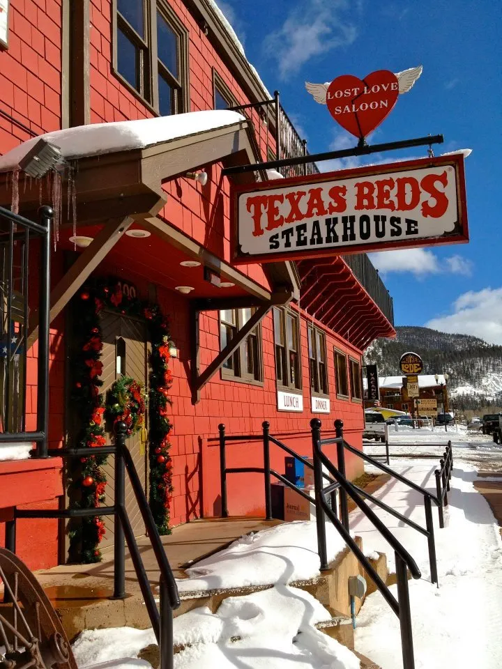 The red Texas Red's Steakhouse building and sign on Main Street in Red River on a snowy day.