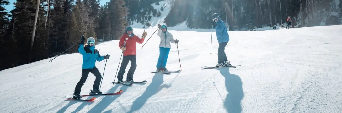 A ski instructor in a red jacket leads a lesson on a groomed slope at Red River Ski and Summer Area.