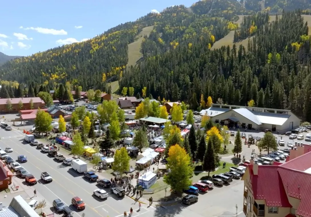 An aerial view of Oktoberfest crowds in Brandenburg Park beneath Red River's ski slopes and golden aspens.