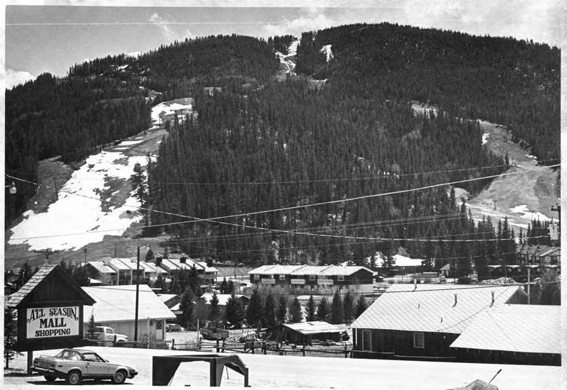 A black-and-white photograph, circa 1980, of Red River's ski slopes rising above the town and the All Season Mall.
